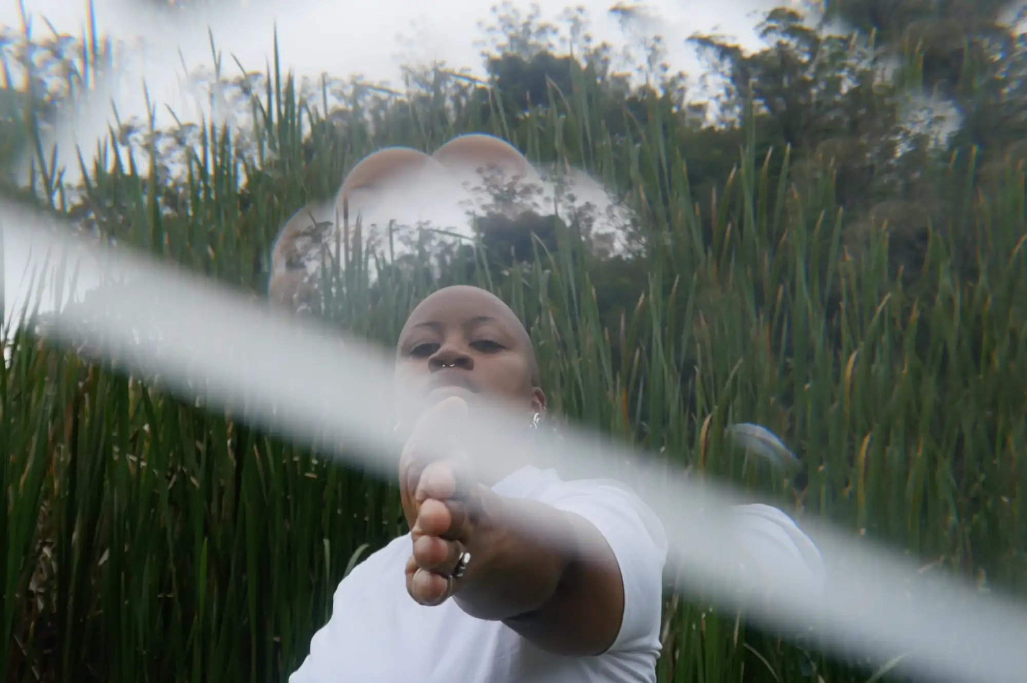 Person steht mittig im hohen Gras und zeigt mit flacher Hand in Richtung des Betrachters