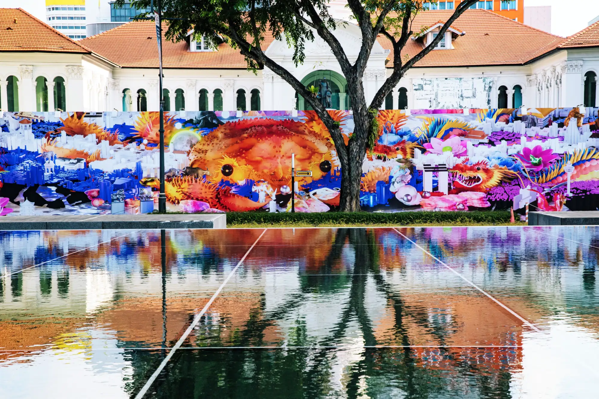 Blick auf eine riesige, bunte Leinwand hinter einer großen Wasserfläche an einem Platz.