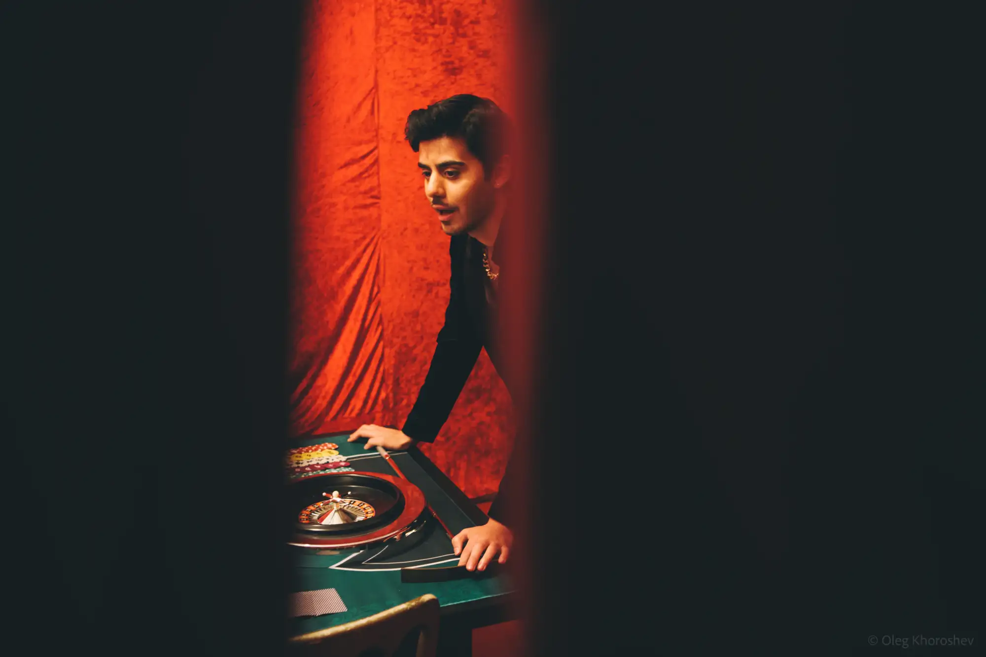 Blick durch einen Spalt im Vorhang: Ein Mann über einen Roulette-Tisch gelehnt.