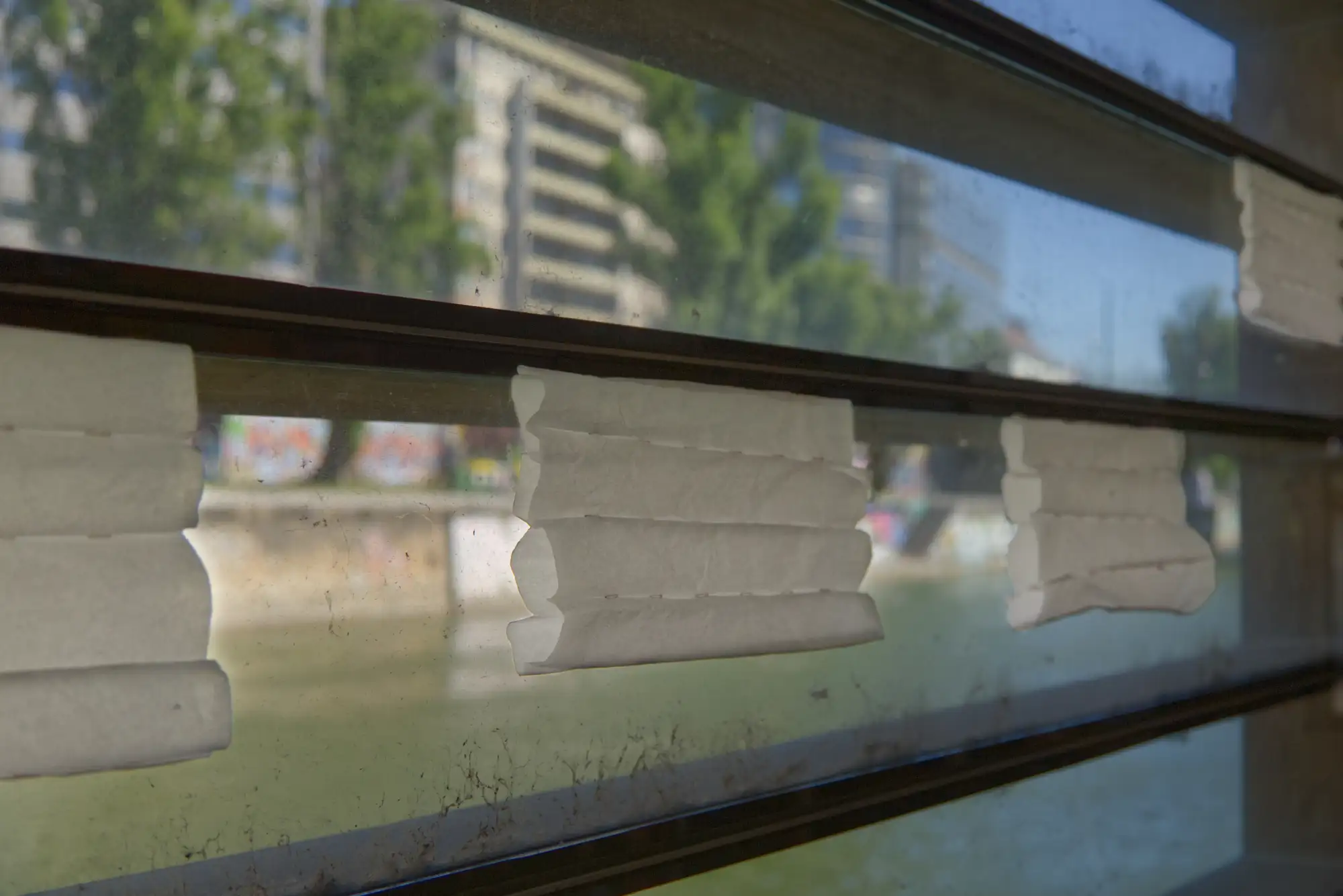 Im Fenster hängen mehrere Stücke Stoff, die so vernäht sind, dass sich waagrechte Röhren bilden.