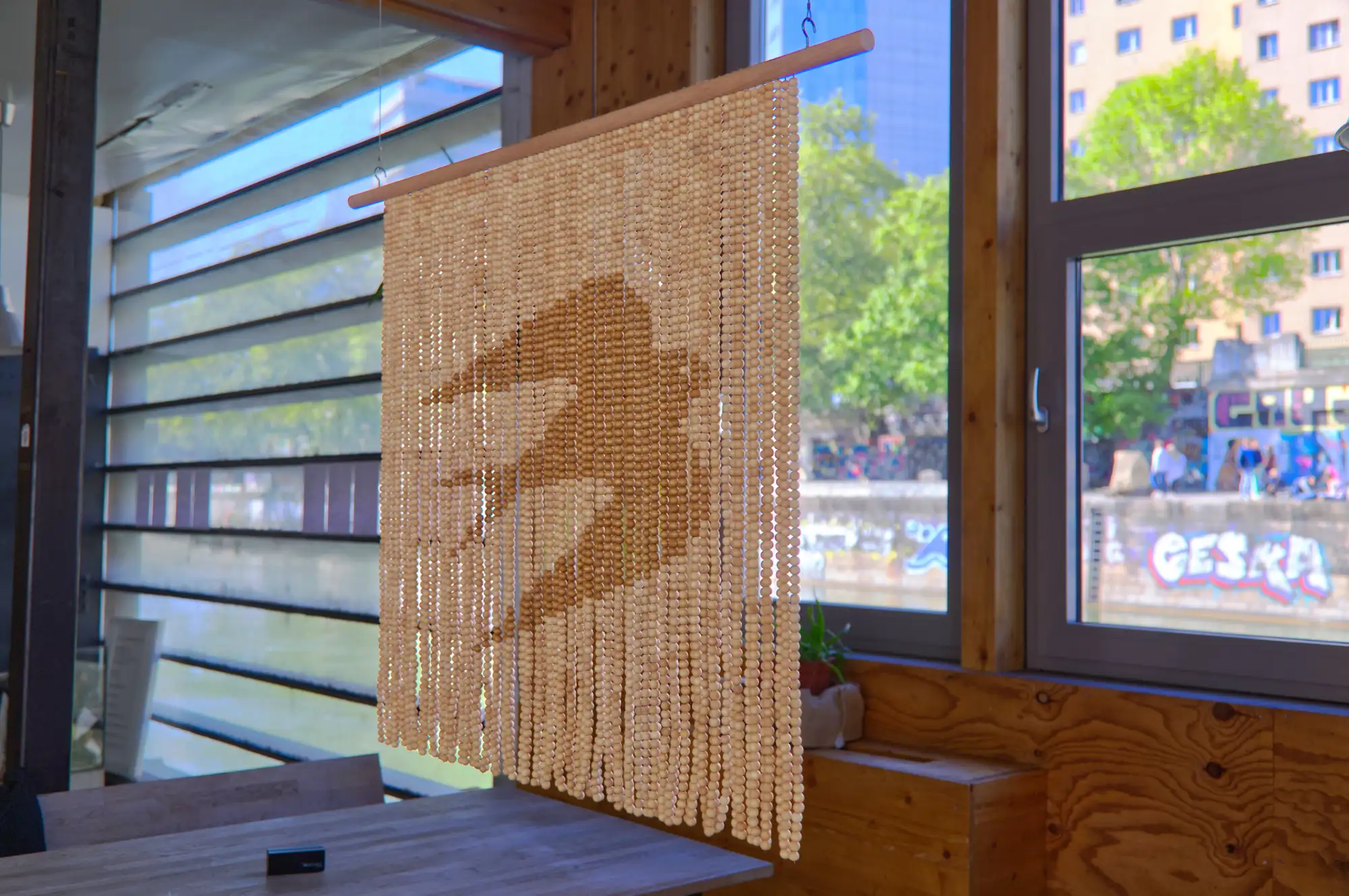 Ein Perlenvorhang, aus dunkel- und hellbraunen Holzperlen, die dunklen zeigen die Silhouette eines fliegenden Vogels.