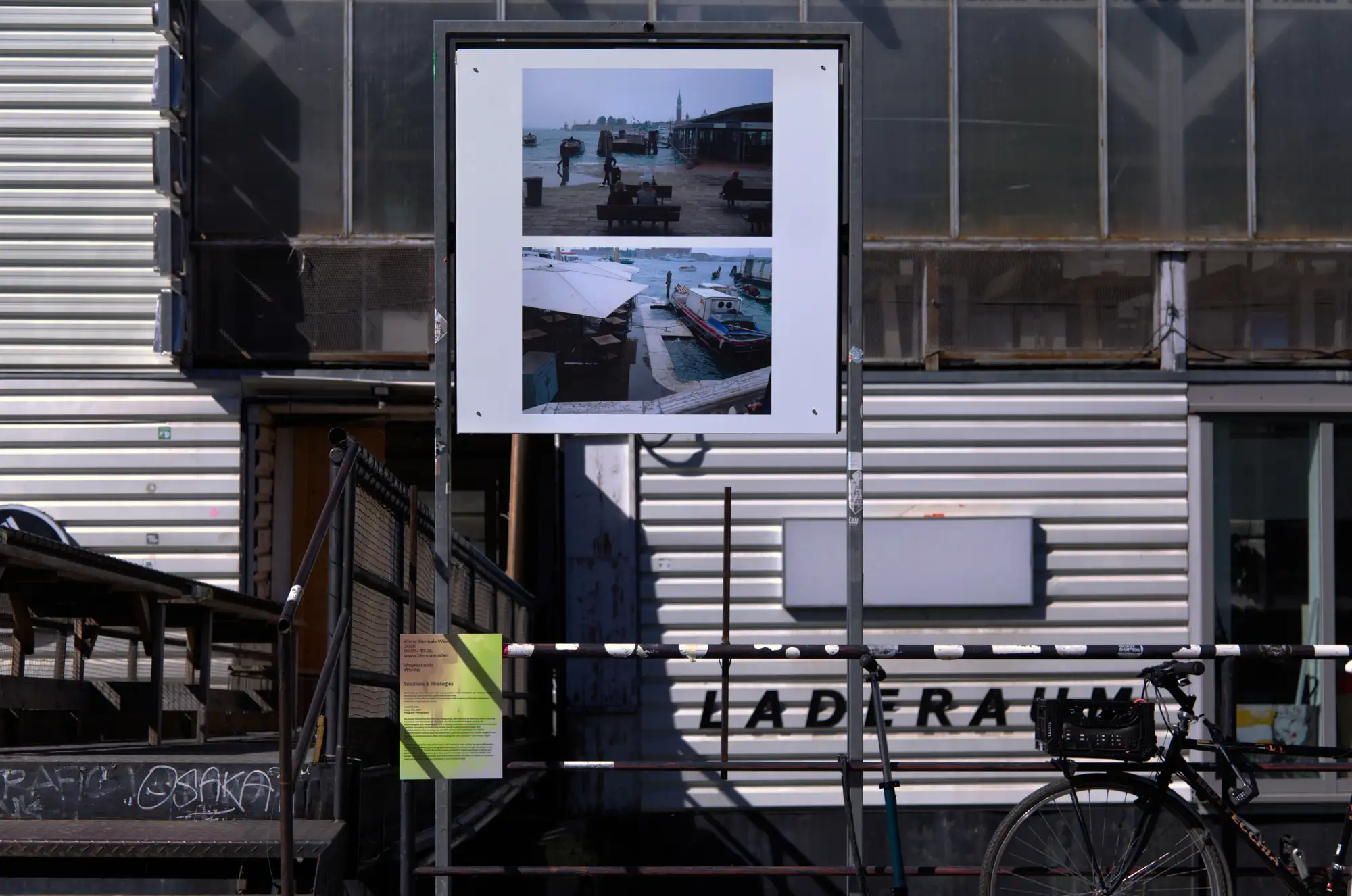 Eine Plakatwand am Pier neben dem Badeschiff, darauf zwei Fotos aus Venedig, während eines Hochwassers.