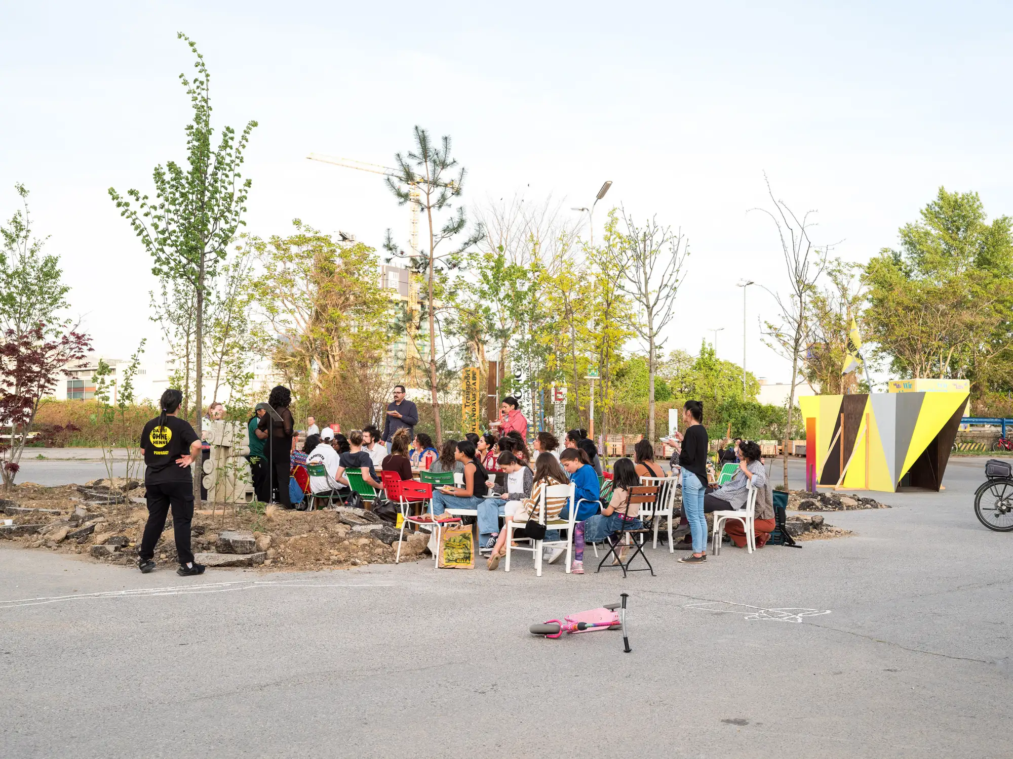 Menschen sitzend auf Stühlen in einem aufgeschütteten Garten auf Betonfläche