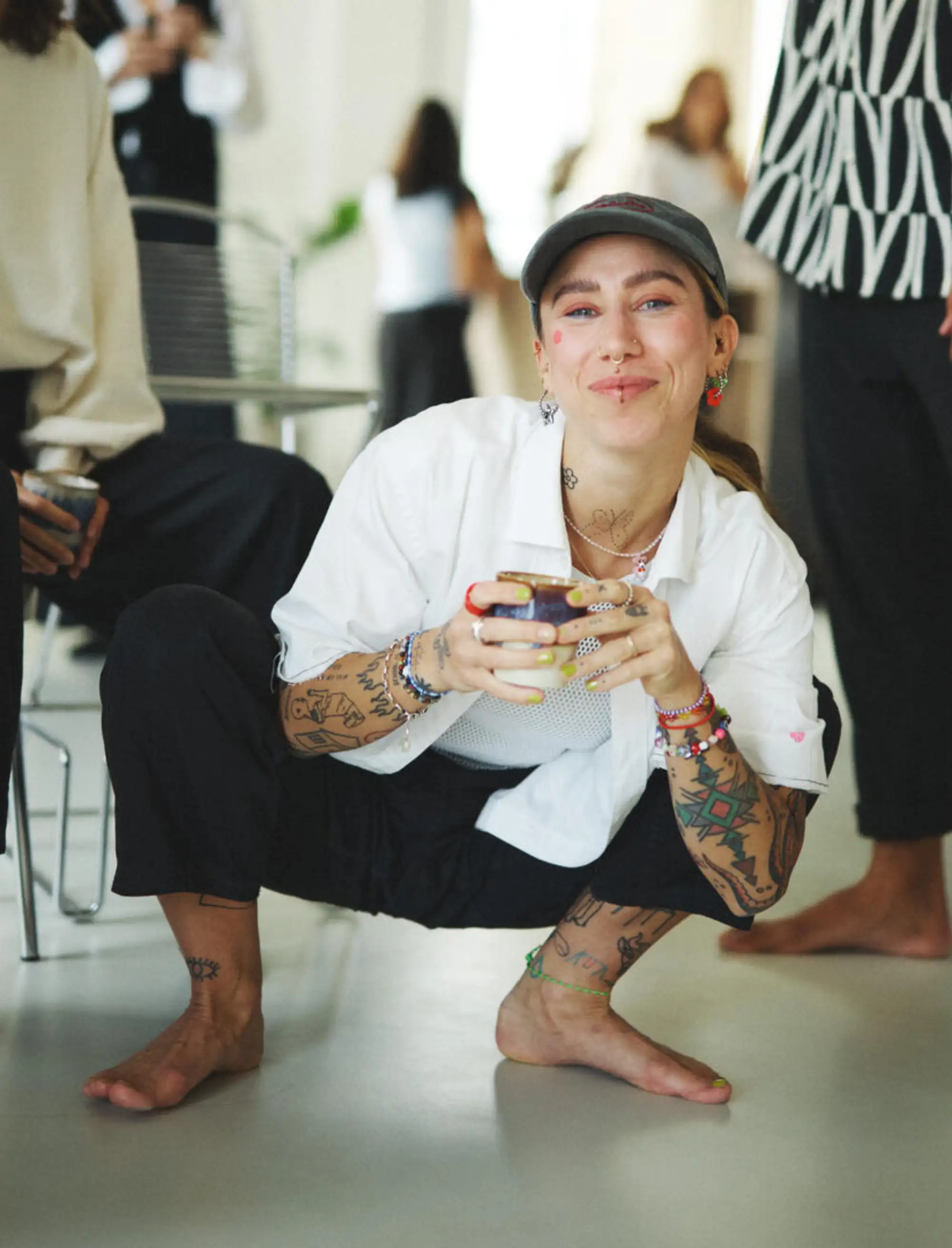 Frau in weißem Shirt und dunkler Hose mit Kappe, hockend