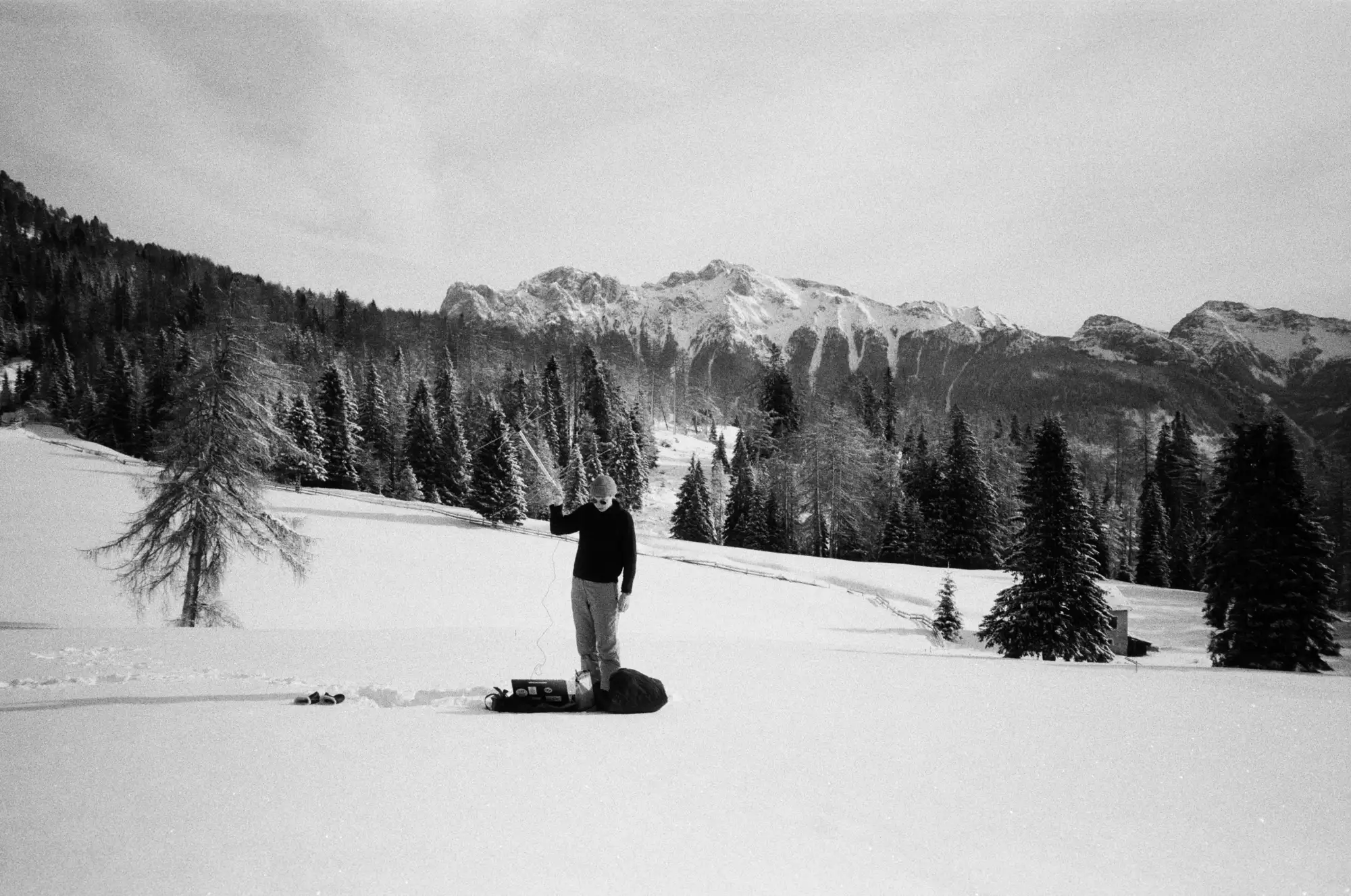 schwarzweißes Foto von verschneiter Berglandschaft, mittig steht eine Person auf einem Snowboard