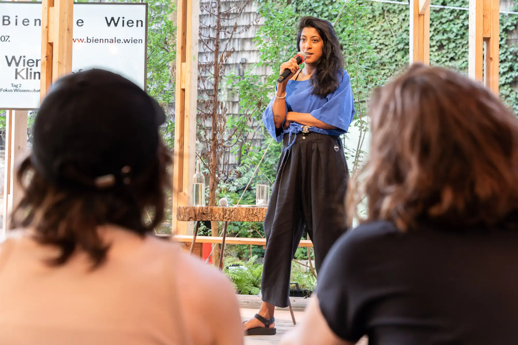 Frau steht auf einer Bühen mit Mikro in der Hand und spricht